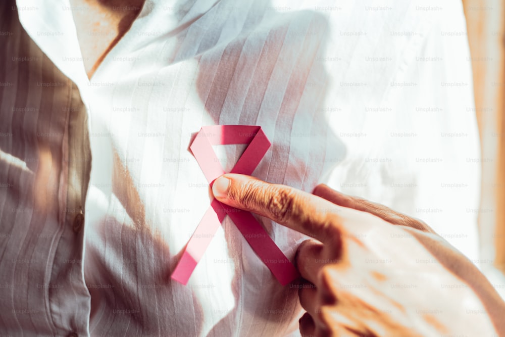 a man is holding a pink ribbon on his shirt