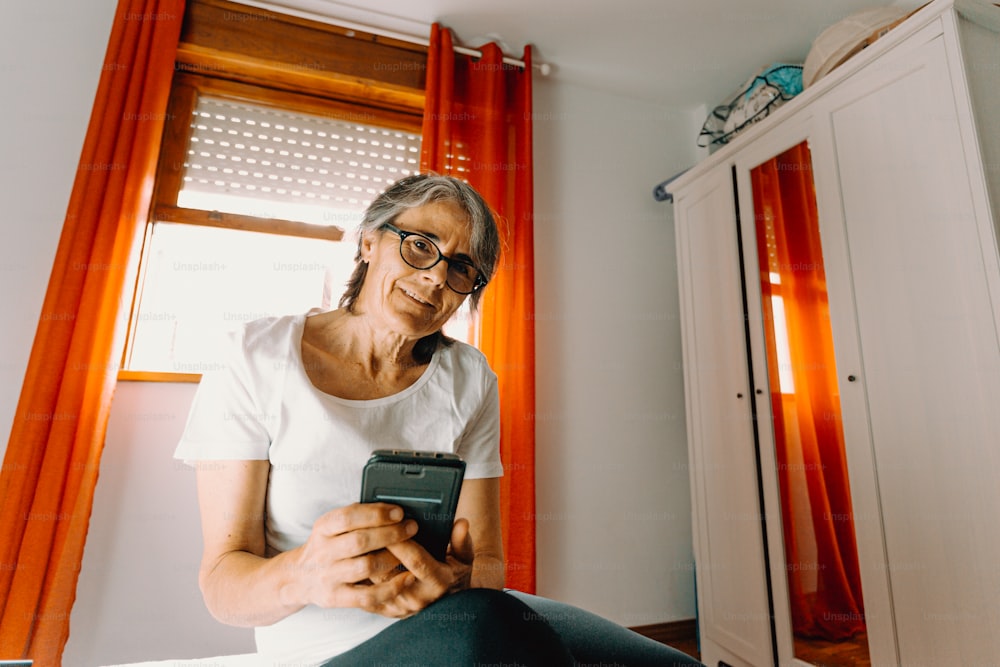 Una mujer sentada en una cama mirando su teléfono celular