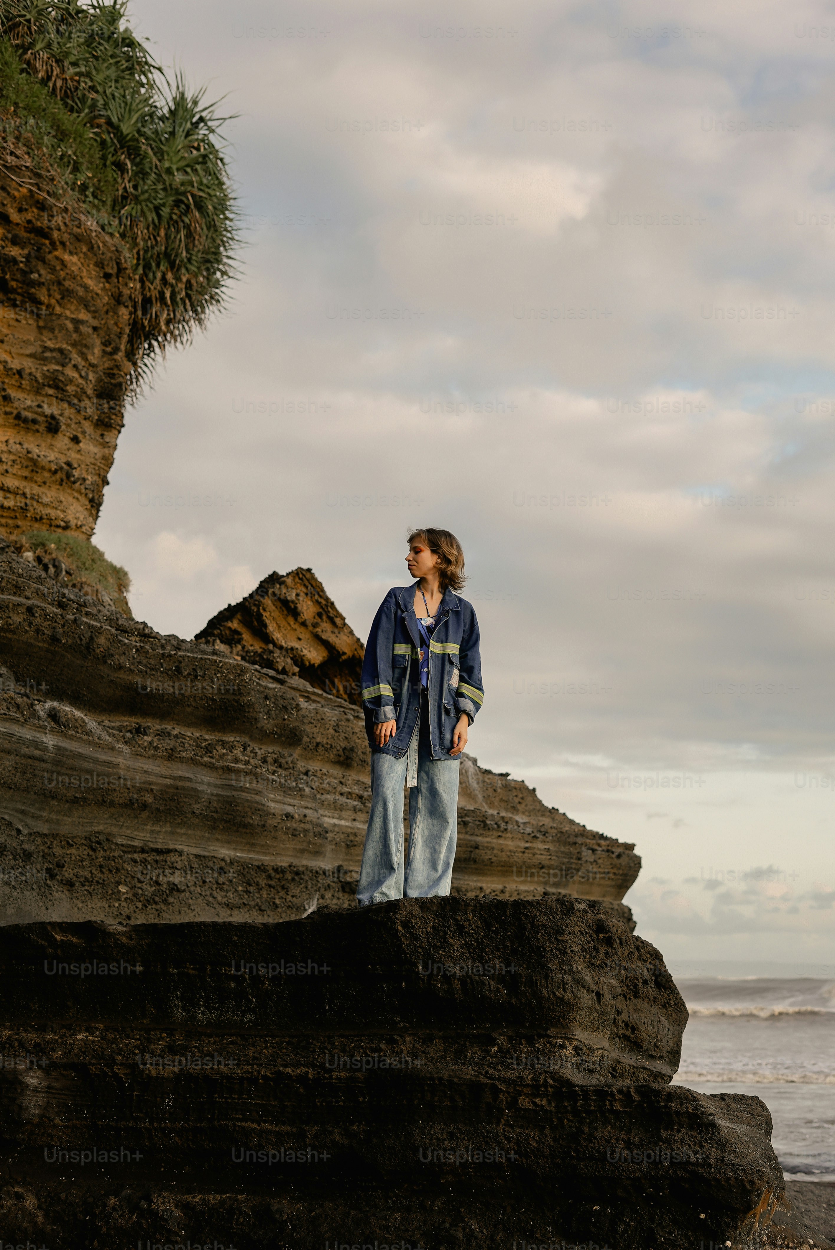 A woman standing on top of a rock near the ocean photo – Beach Image on ...