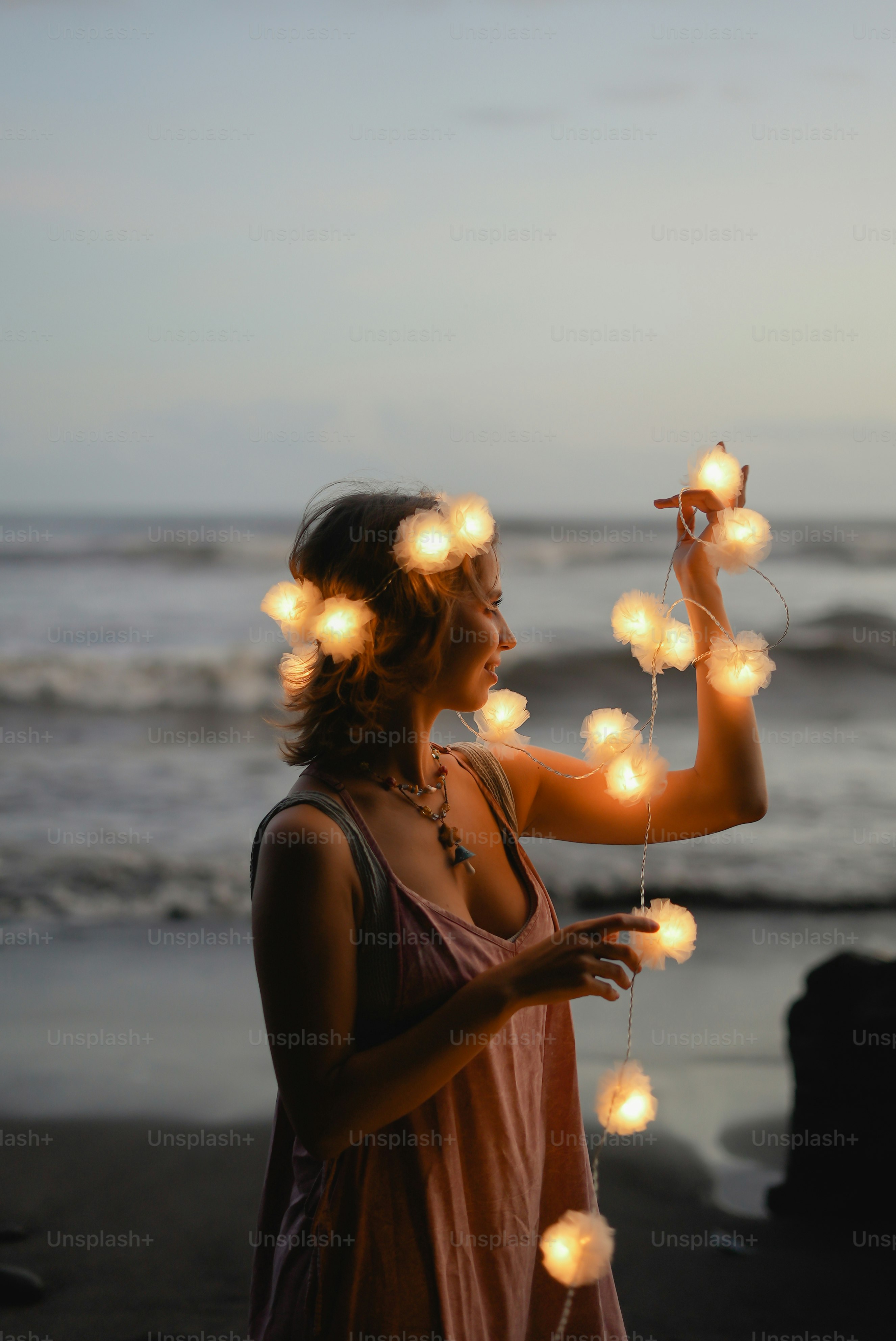 a woman standing on a beach holding a string of lights