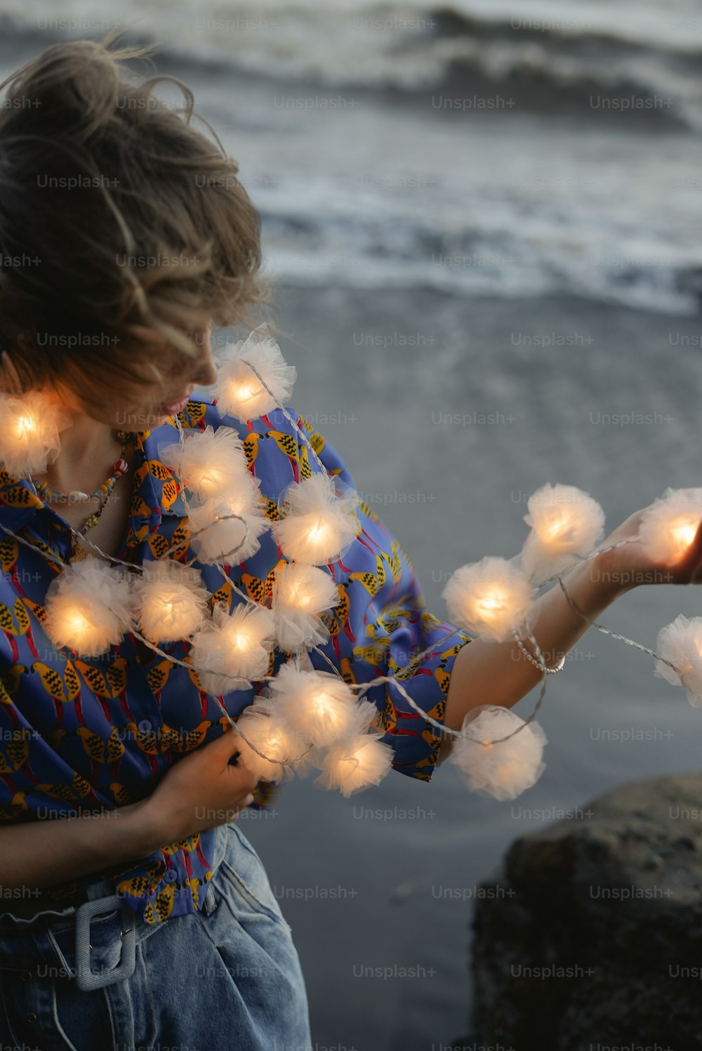 a young girl holding a string of lights near the ocean
