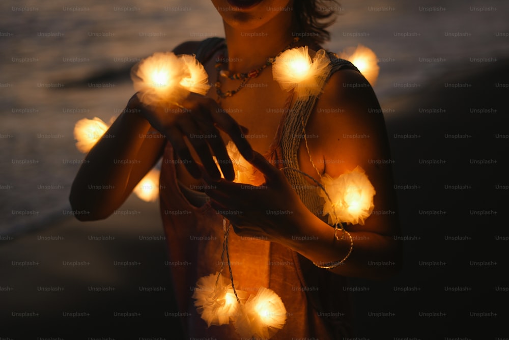 Una mujer parada en una playa sosteniendo una cadena de luces