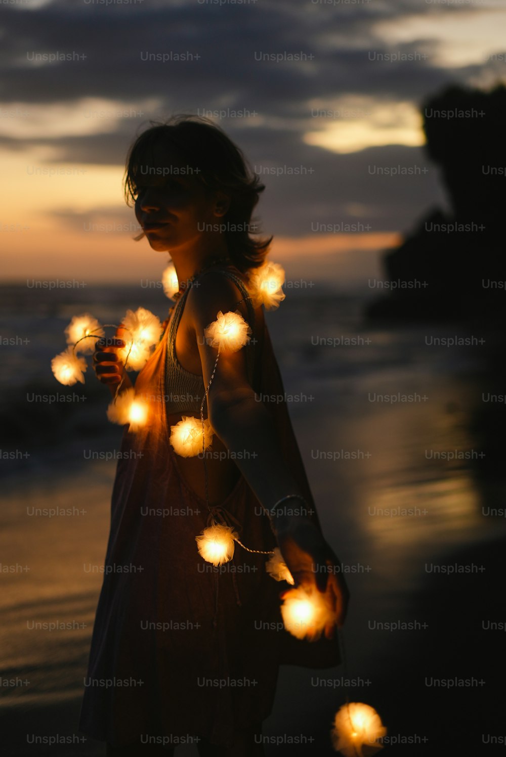 a woman standing on a beach holding a string of lights