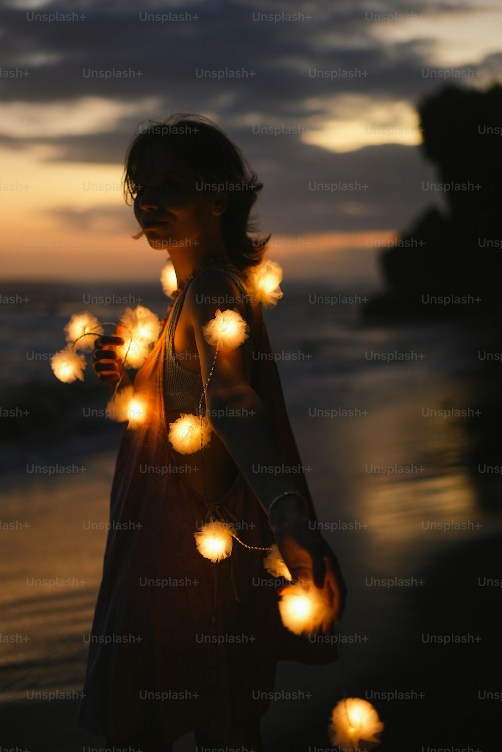 Una mujer parada en una playa sosteniendo una cadena de luces