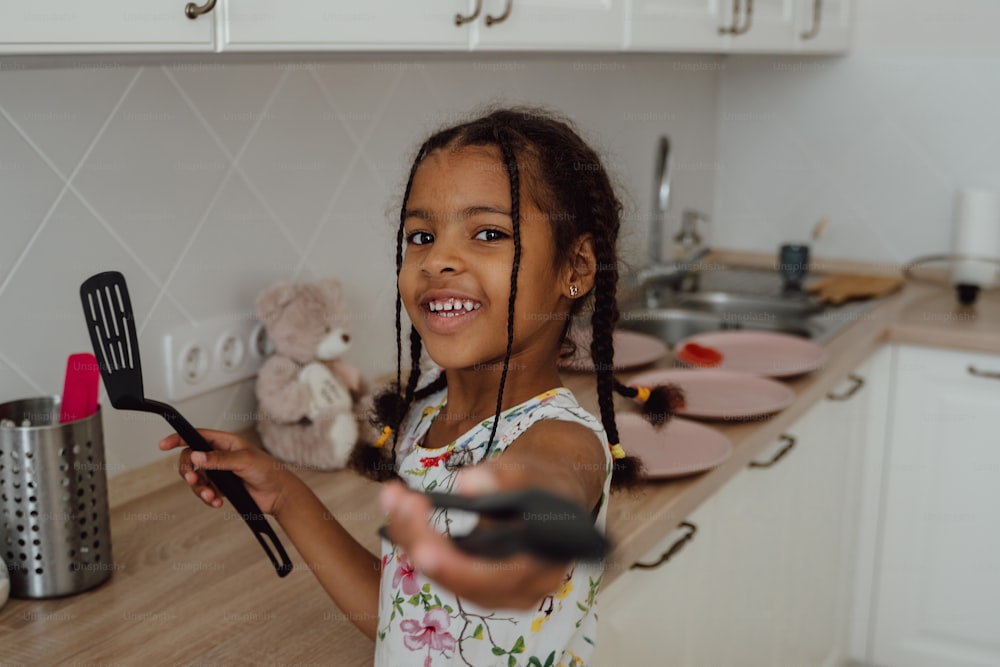 a little girl holding a spatula in a kitchen