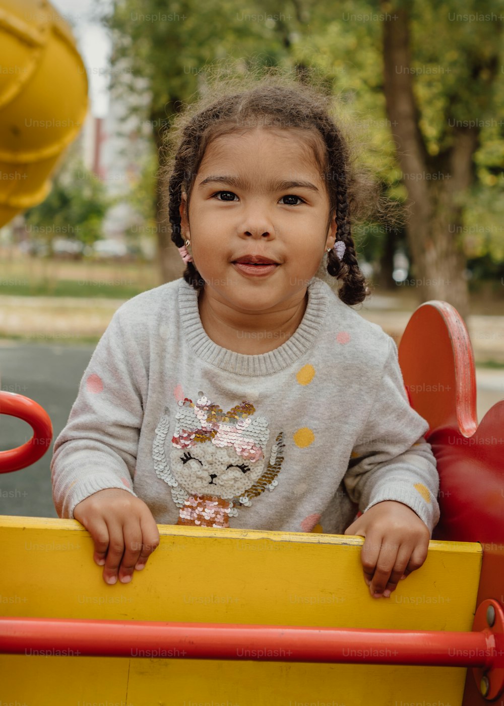 Ein kleines Mädchen, das in einem gelben Spielzeugauto sitzt
