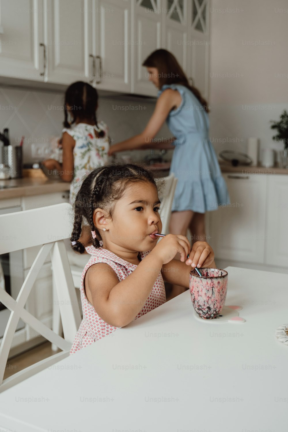 a little girl sitting at a table with a cup