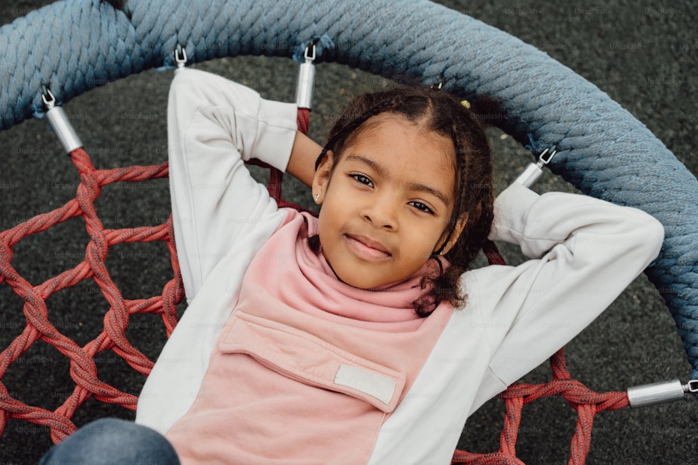 a little girl sitting in a hammock with her hands on her head