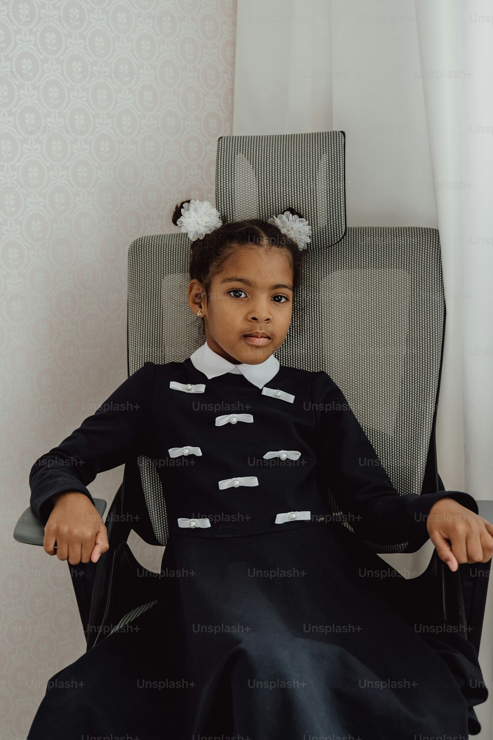 a little girl sitting in a chair wearing a black dress
