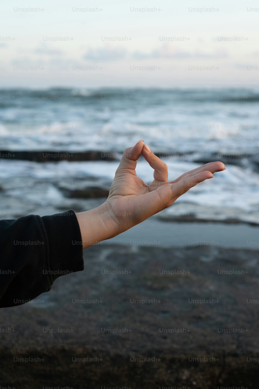 a person holding out their hand in front of the ocean