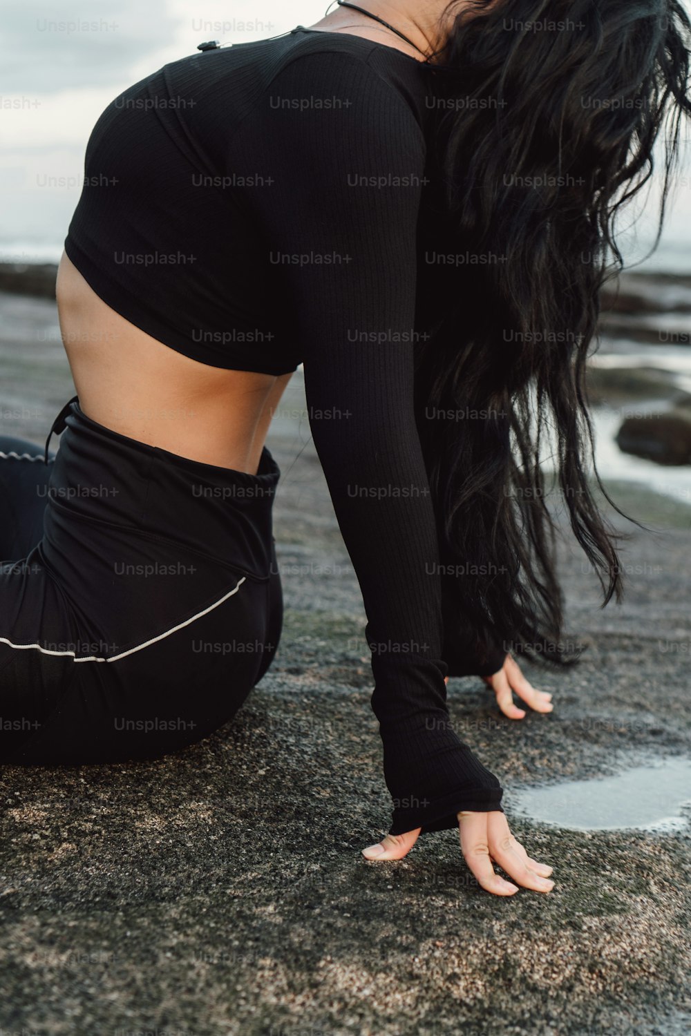 a woman in a black top and leggings on a beach