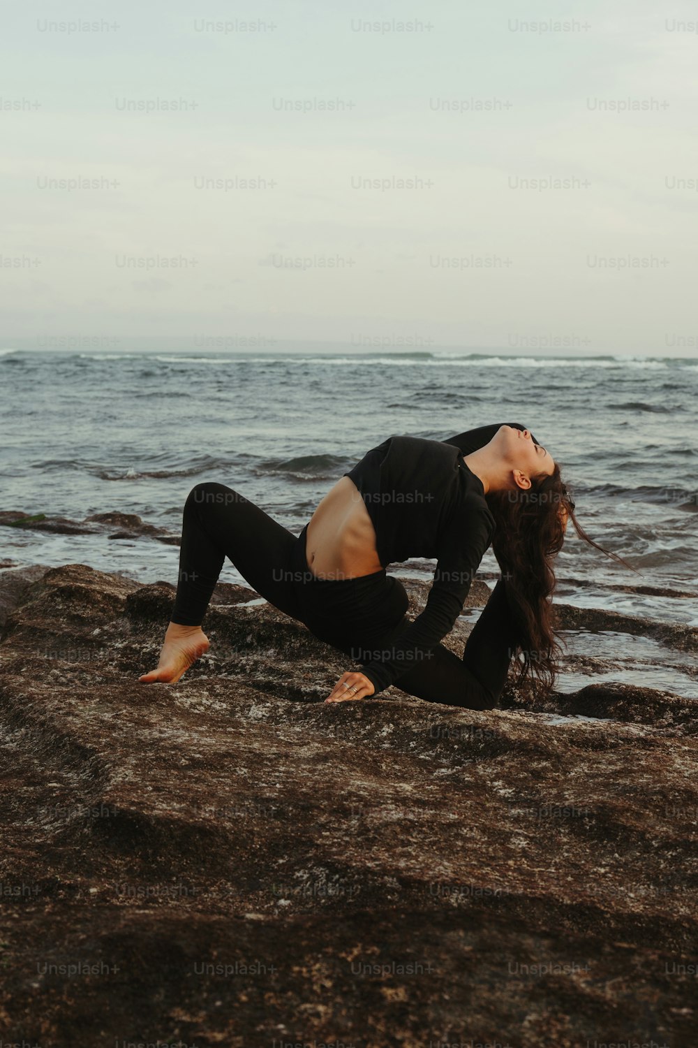 a woman in a black top and leggings on a rocky beach