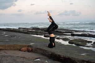 a woman doing a handstand in front of the ocean