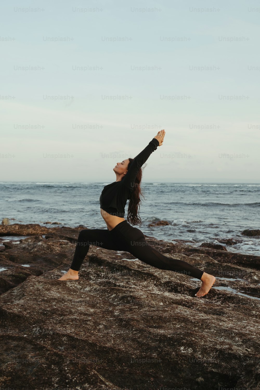 Une femme faisant une pose de yoga sur un rocher au bord de l’océan