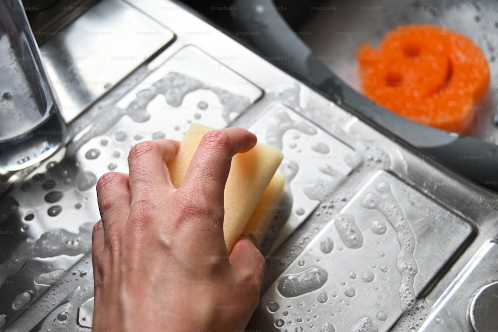 Una persona está limpiando un fregadero de cocina con una esponja