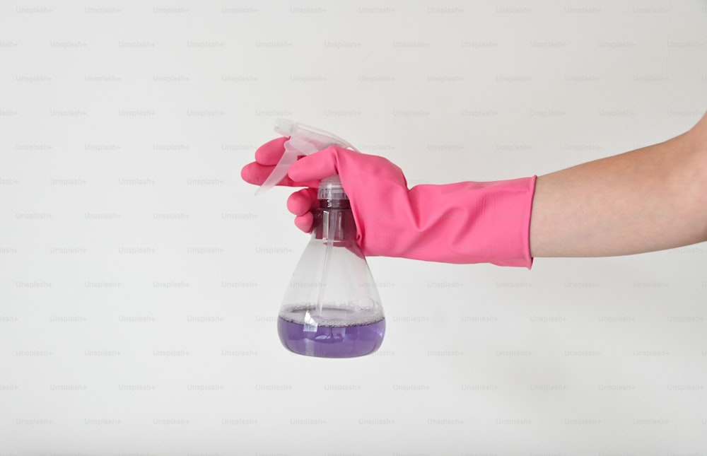 a person in pink gloves holding a purple substance in a flask