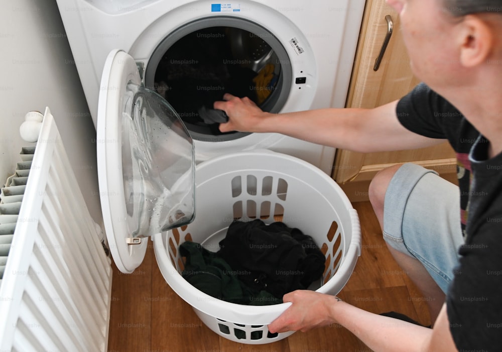 Un hombre está poniendo ropa en una lavadora