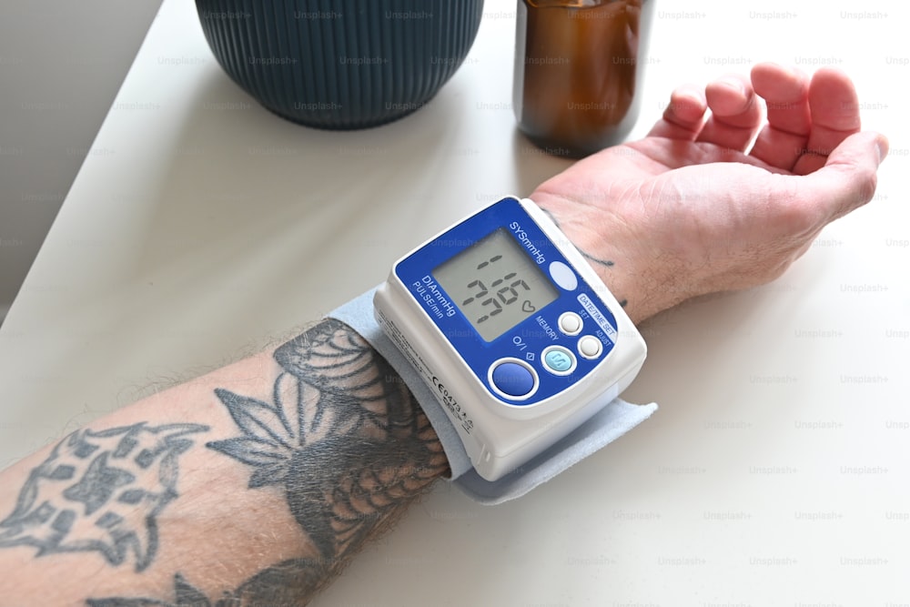 una persona con un tatuaggio sul braccio che tiene un monitor della pressione sanguigna