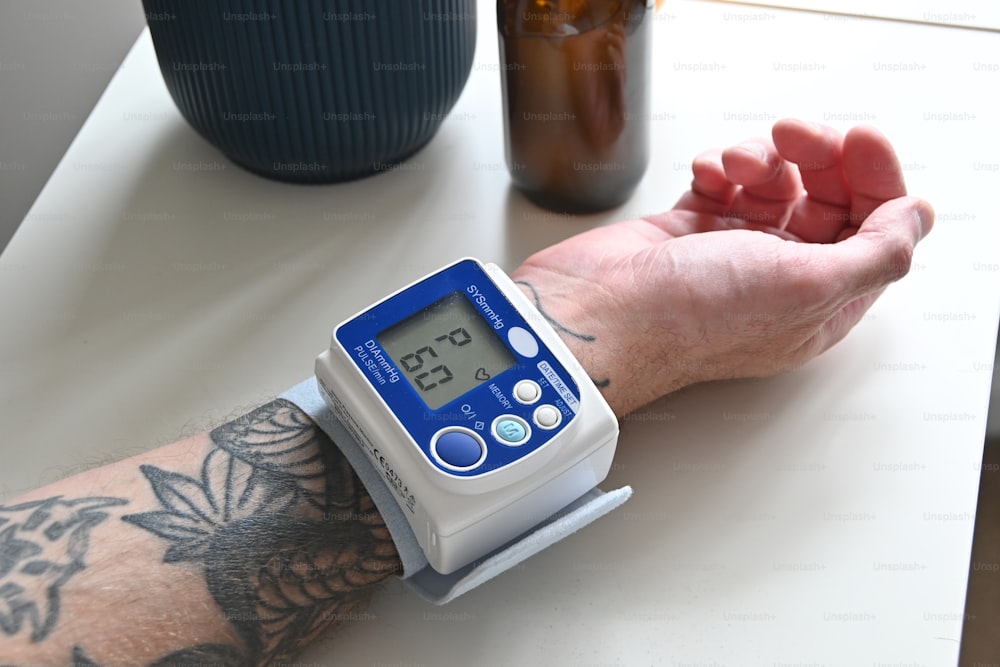 una persona con un tatuaje en el brazo sosteniendo un monitor de presión arterial