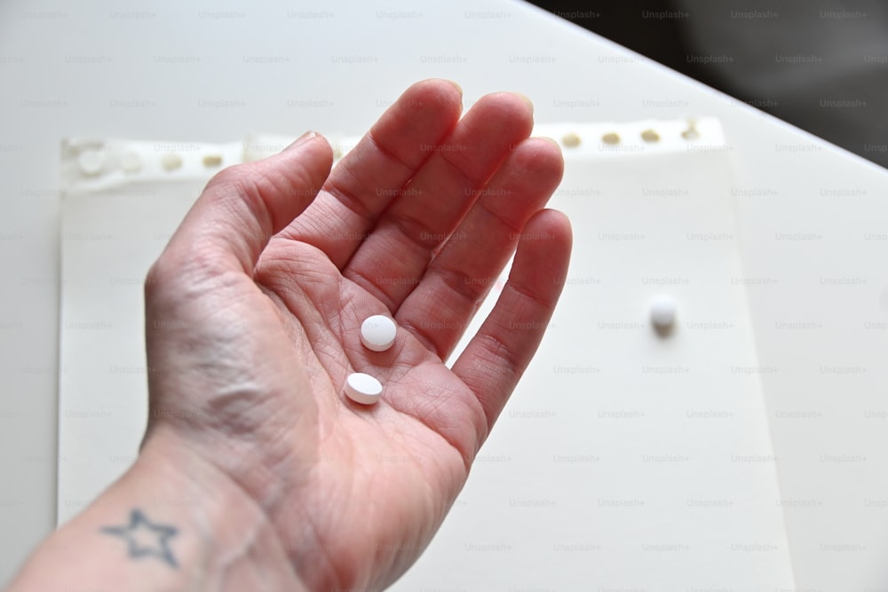 a person's hand holding a small white pill