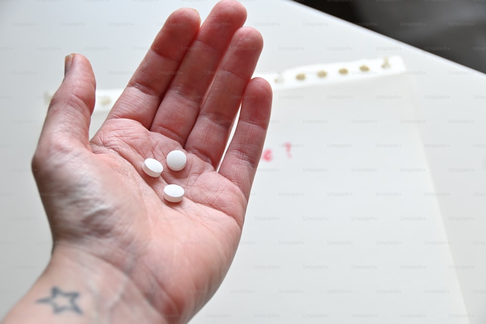 a person's hand holding three white pills