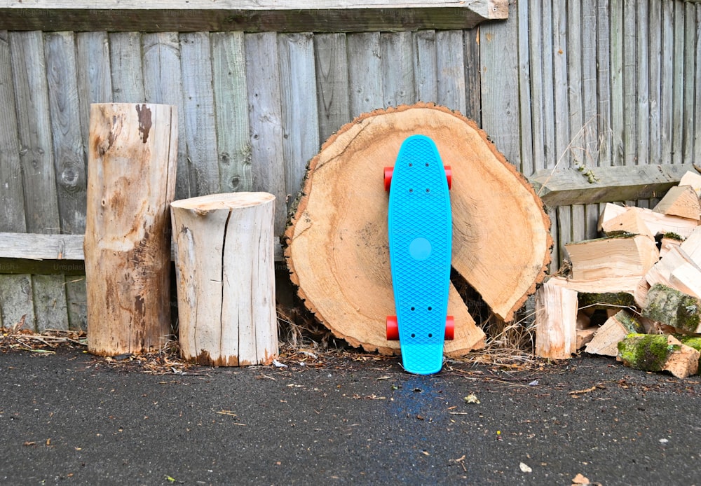 Un monopatín azul apoyado contra un montón de madera