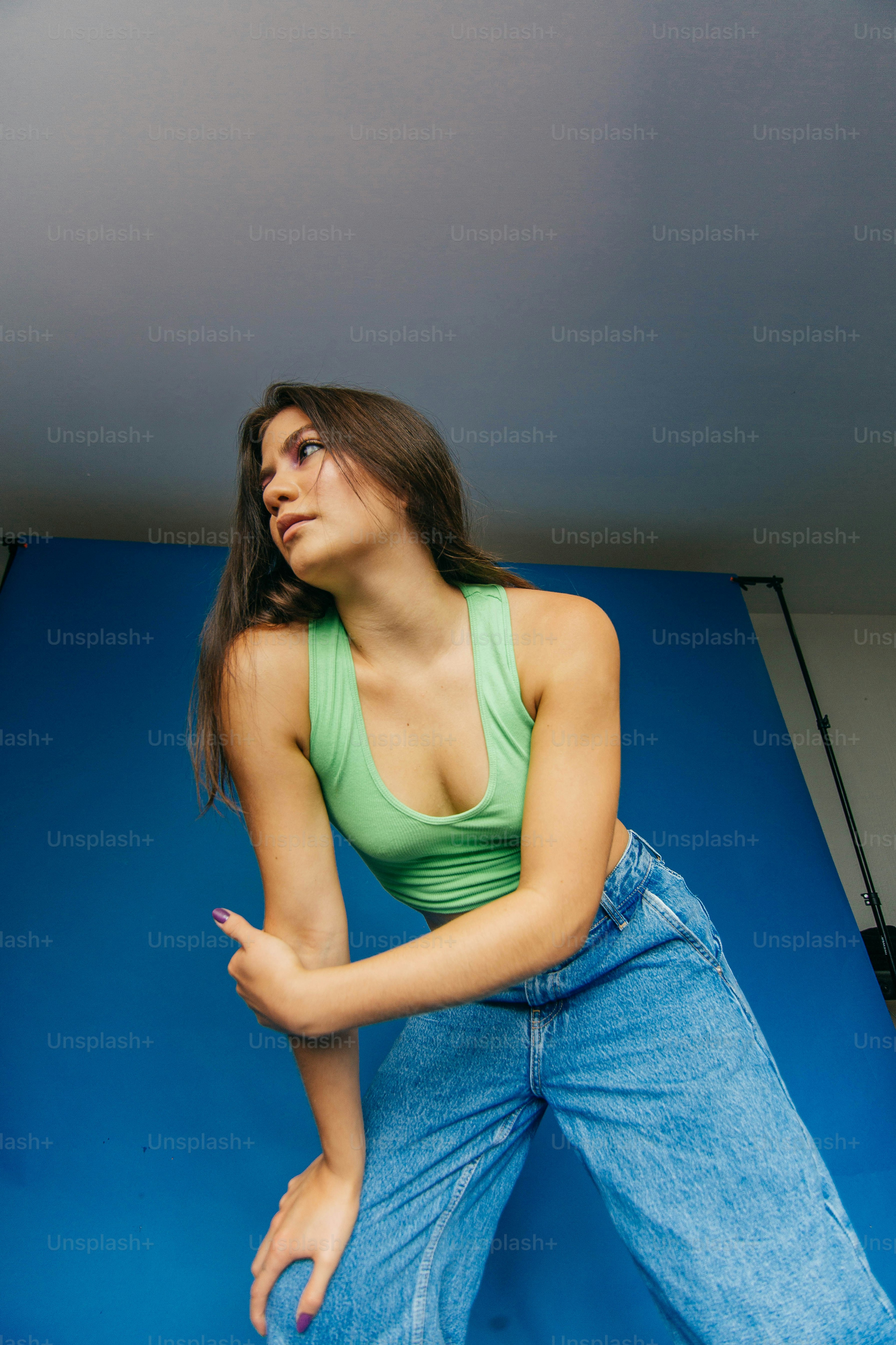 Une femme en débardeur vert appuyée sur un mur bleu