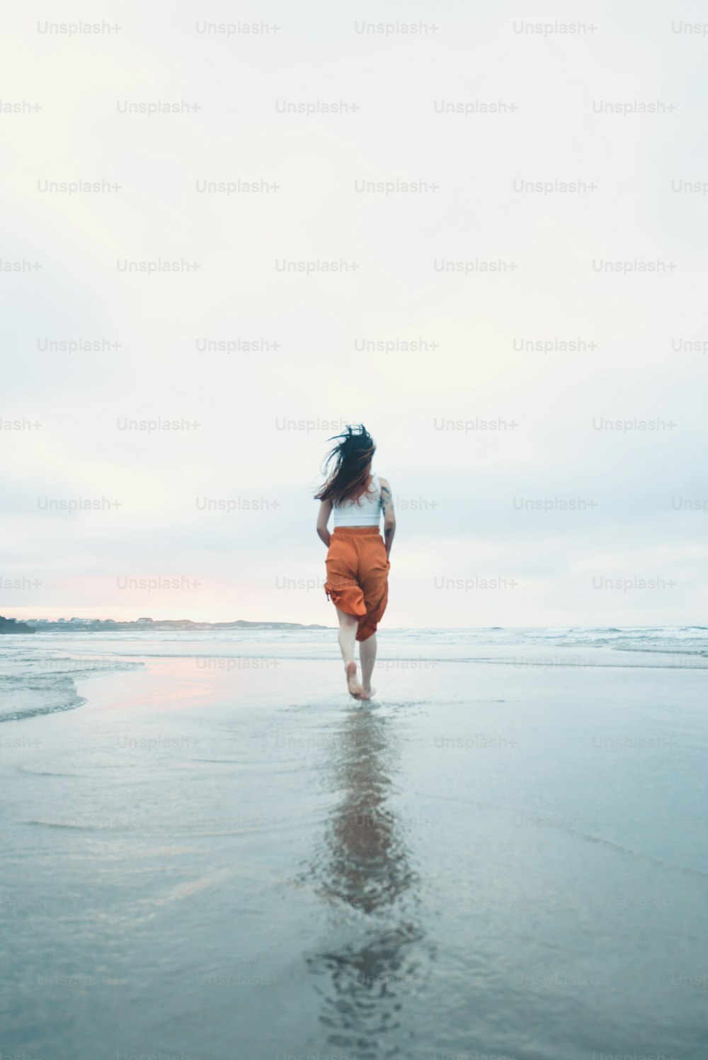 Una mujer corriendo por la playa con el pelo soplando al viento