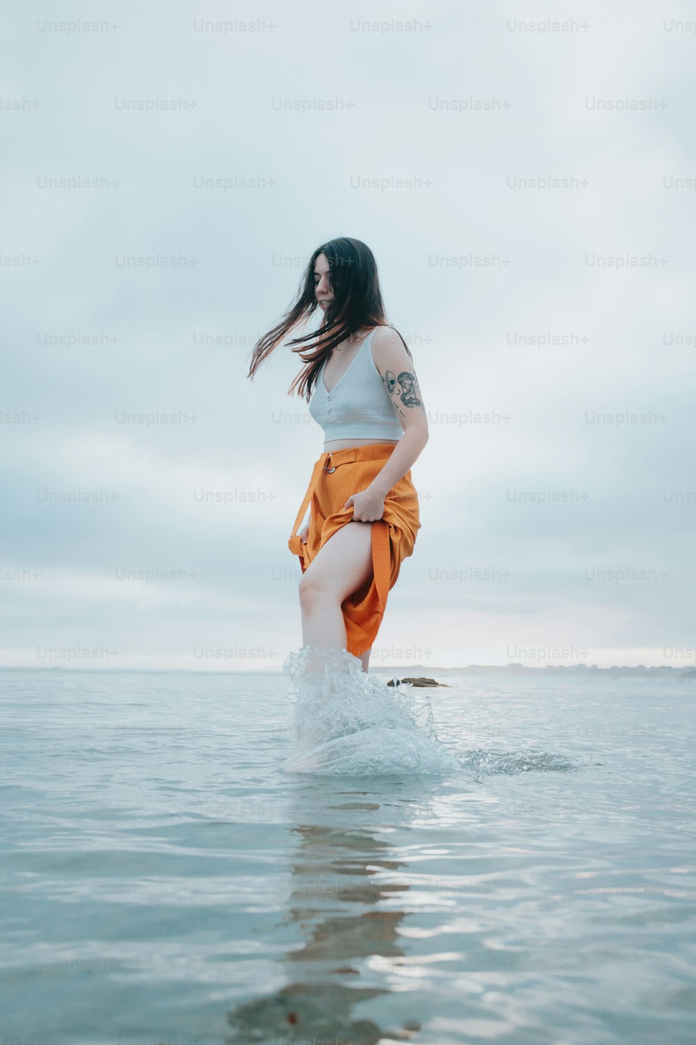 a woman standing in the water with her hair blowing in the wind