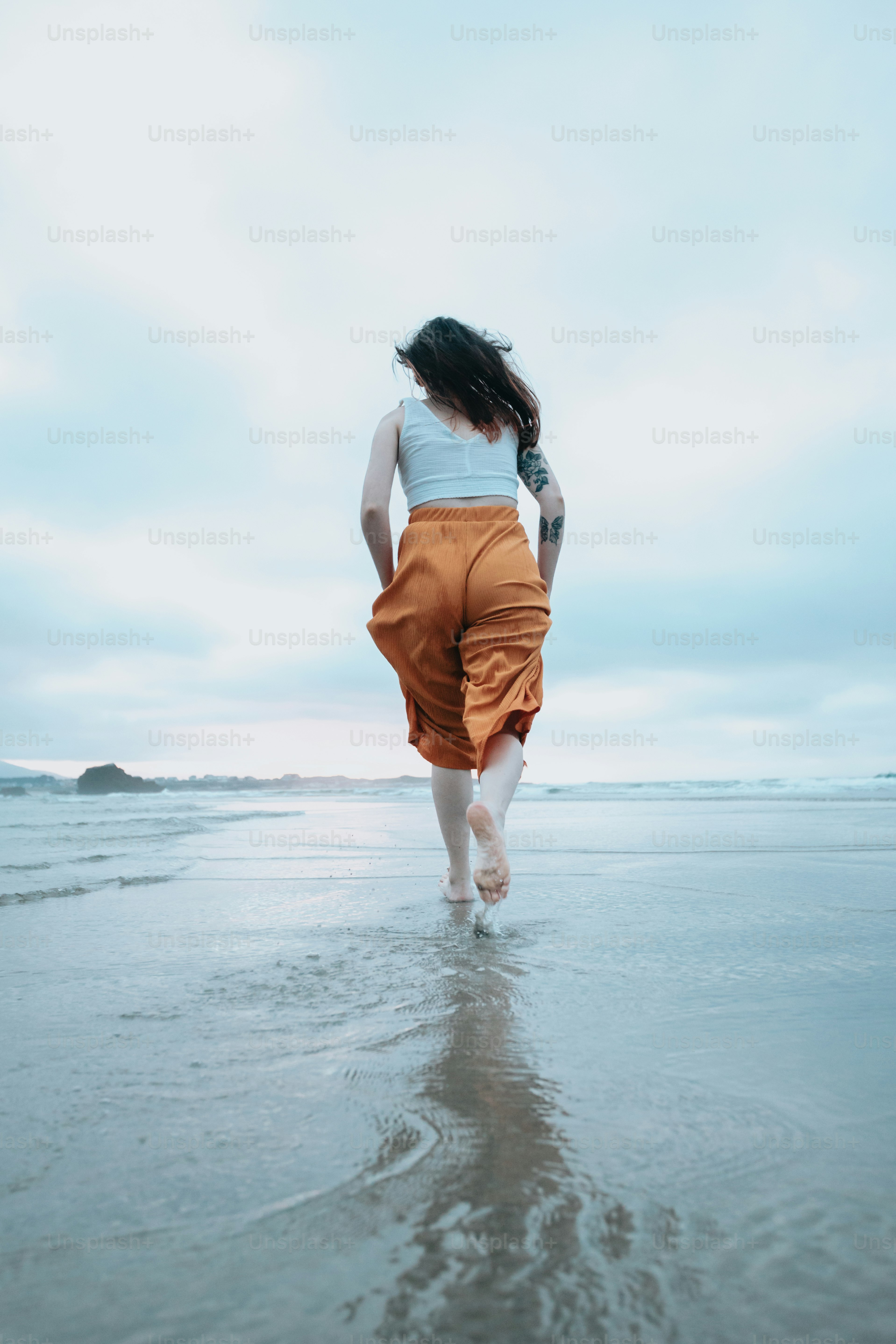 A woman walking along a beach next to the ocean photo – Beach Image on ...
