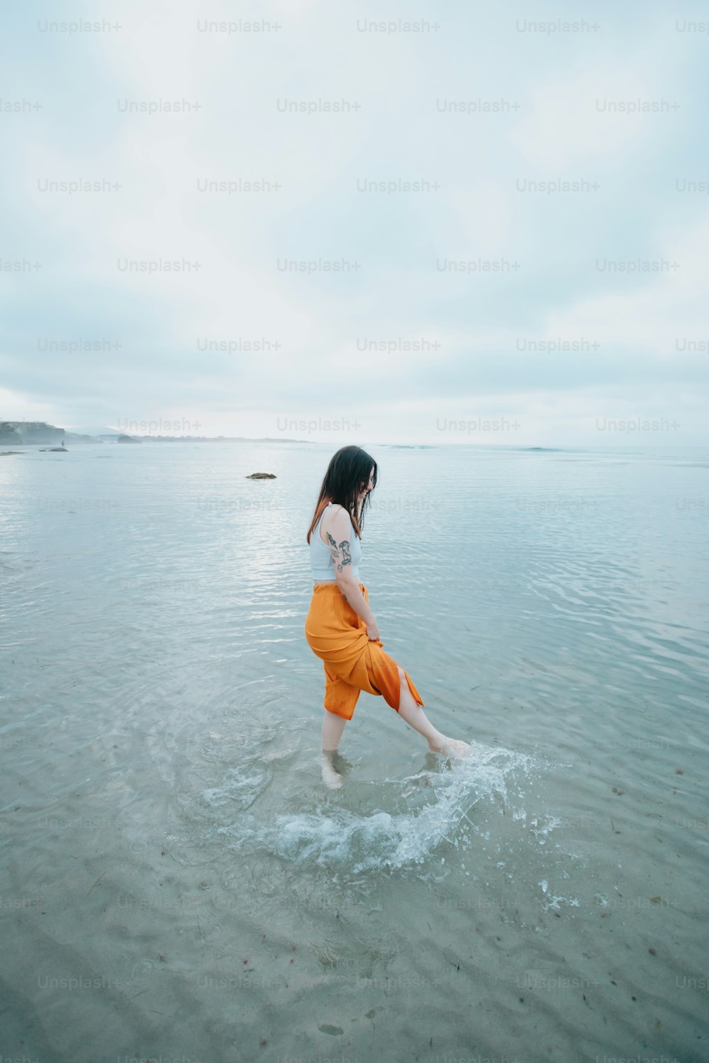 a woman in a white top and orange pants walking in the water