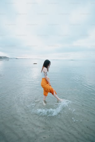 Eine Frau in einem weißen Oberteil und einer orangefarbenen Hose geht im Wasser spazieren