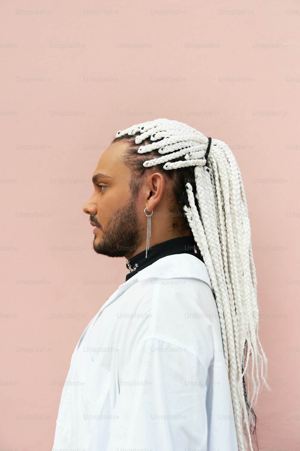 a man with dreadlocks standing against a pink wall