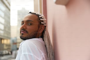 a man leaning against a pink wall with his hair in a bun