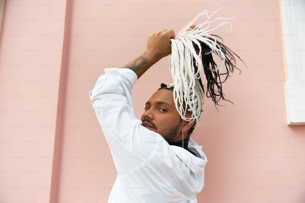 a man with dreadlocks standing in front of a pink wall