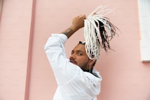 a man with dreadlocks standing in front of a pink wall