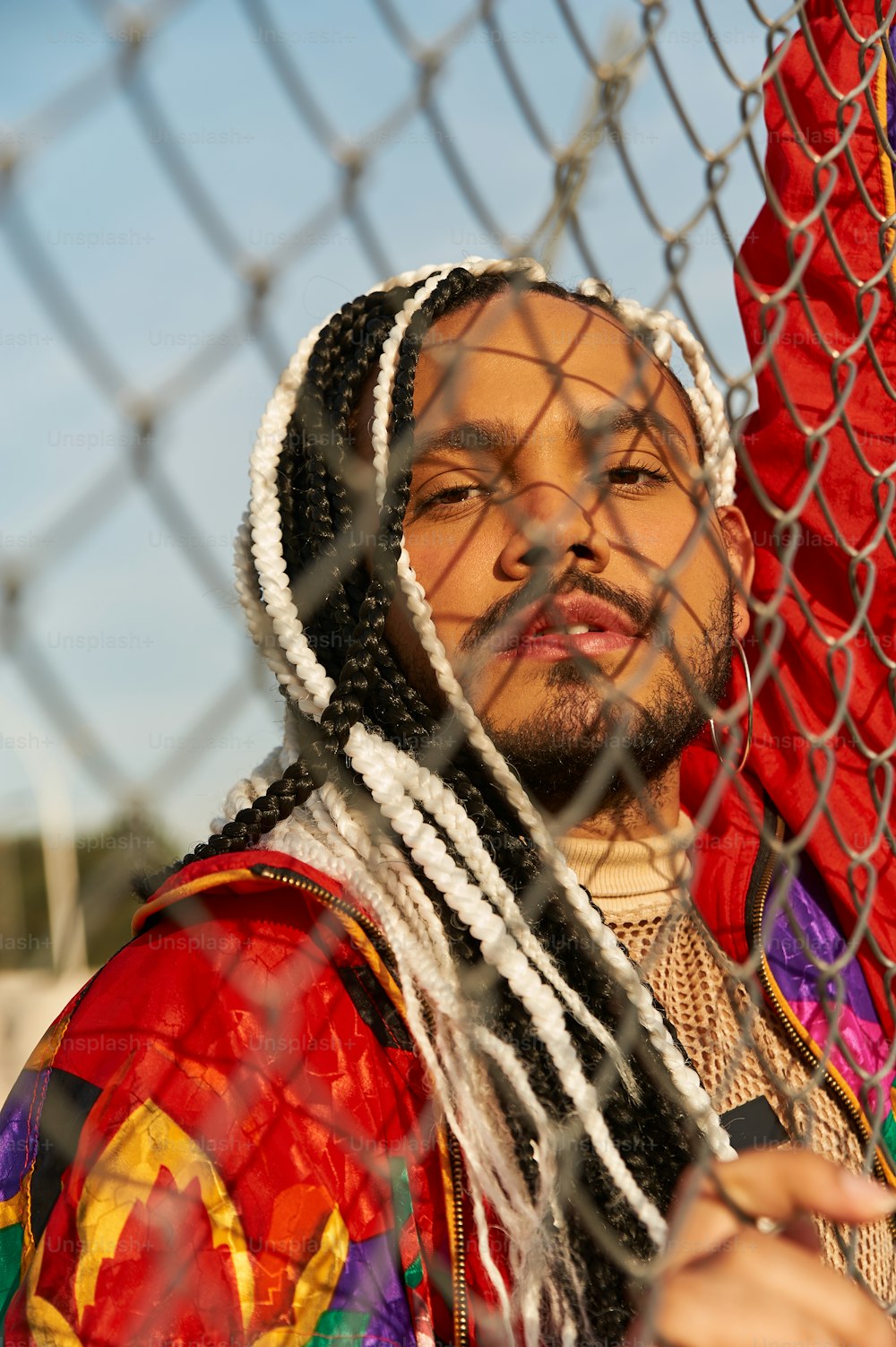 a man with dreadlocks standing behind a chain link fence