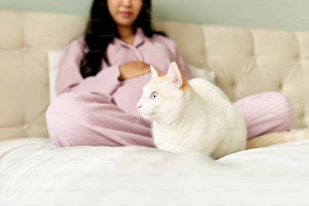 uma mulher sentada em uma cama ao lado de um gato branco