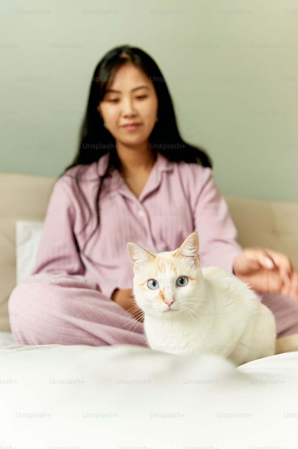 uma mulher sentada em uma cama com um gato branco