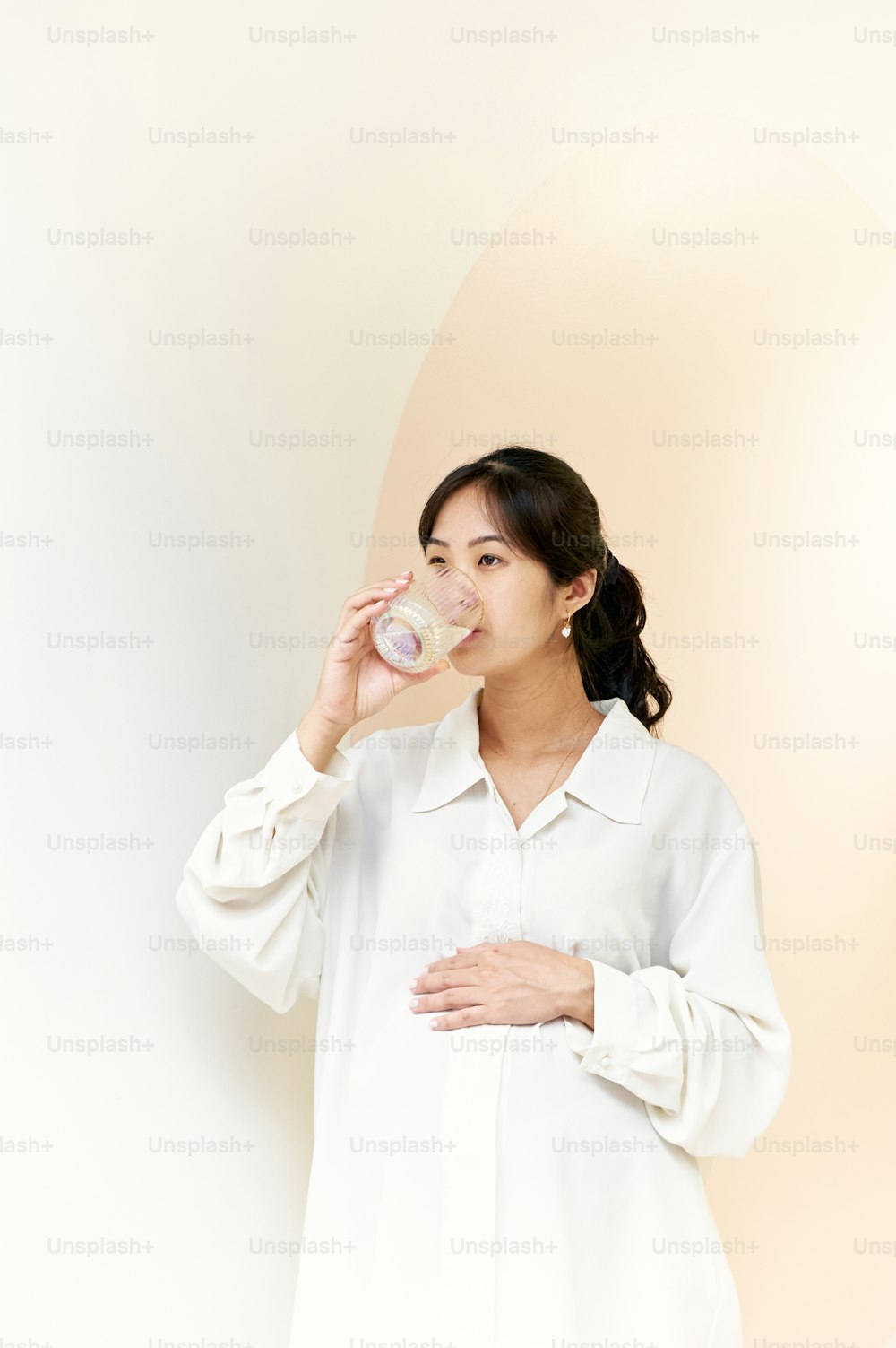 una donna in una camicia bianca che beve da un bicchiere
