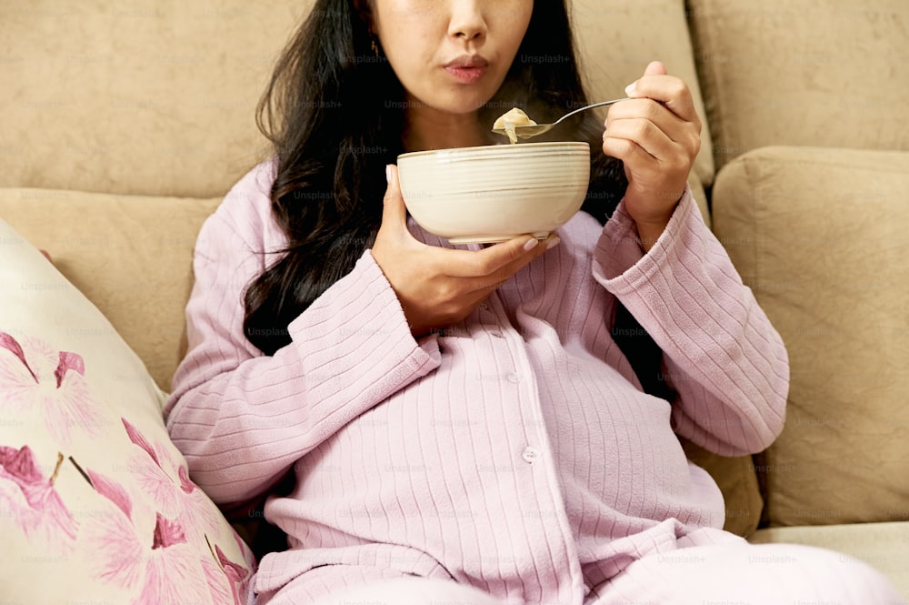 uma mulher sentada em um sofá comendo uma tigela de comida