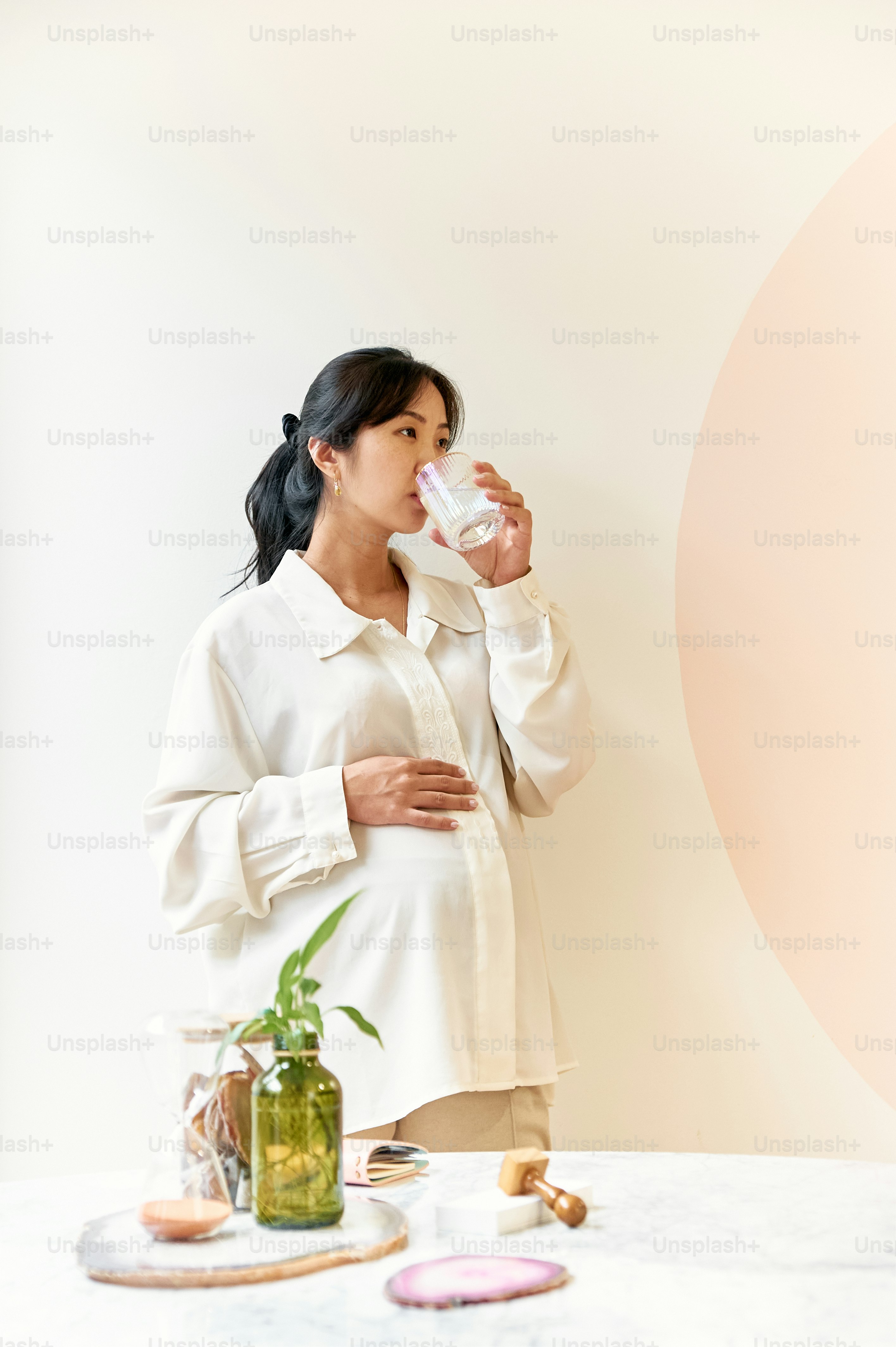 a woman standing in front of a table drinking from a cup