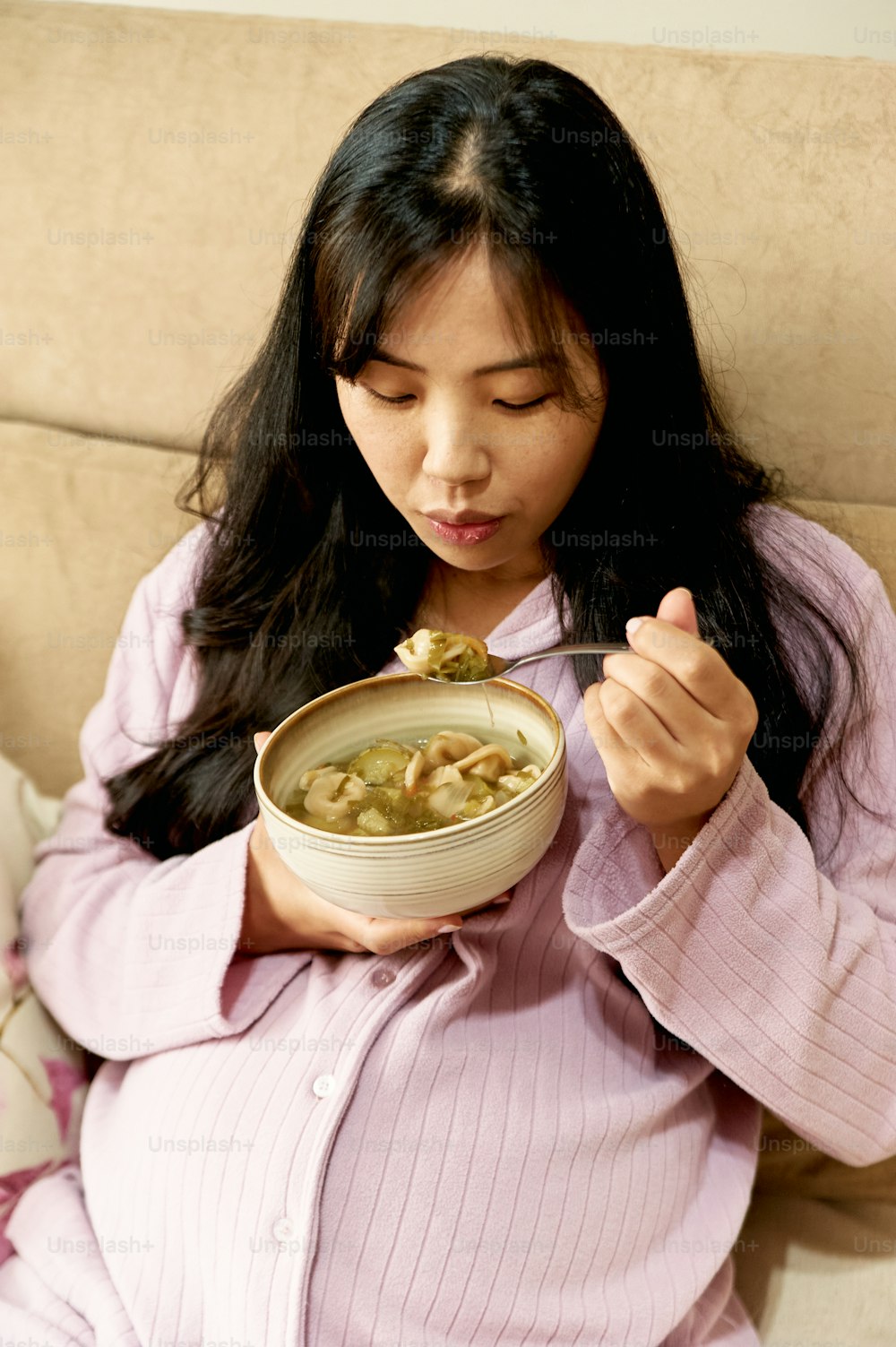 Una mujer sentada en un sofá comiendo un plato de sopa