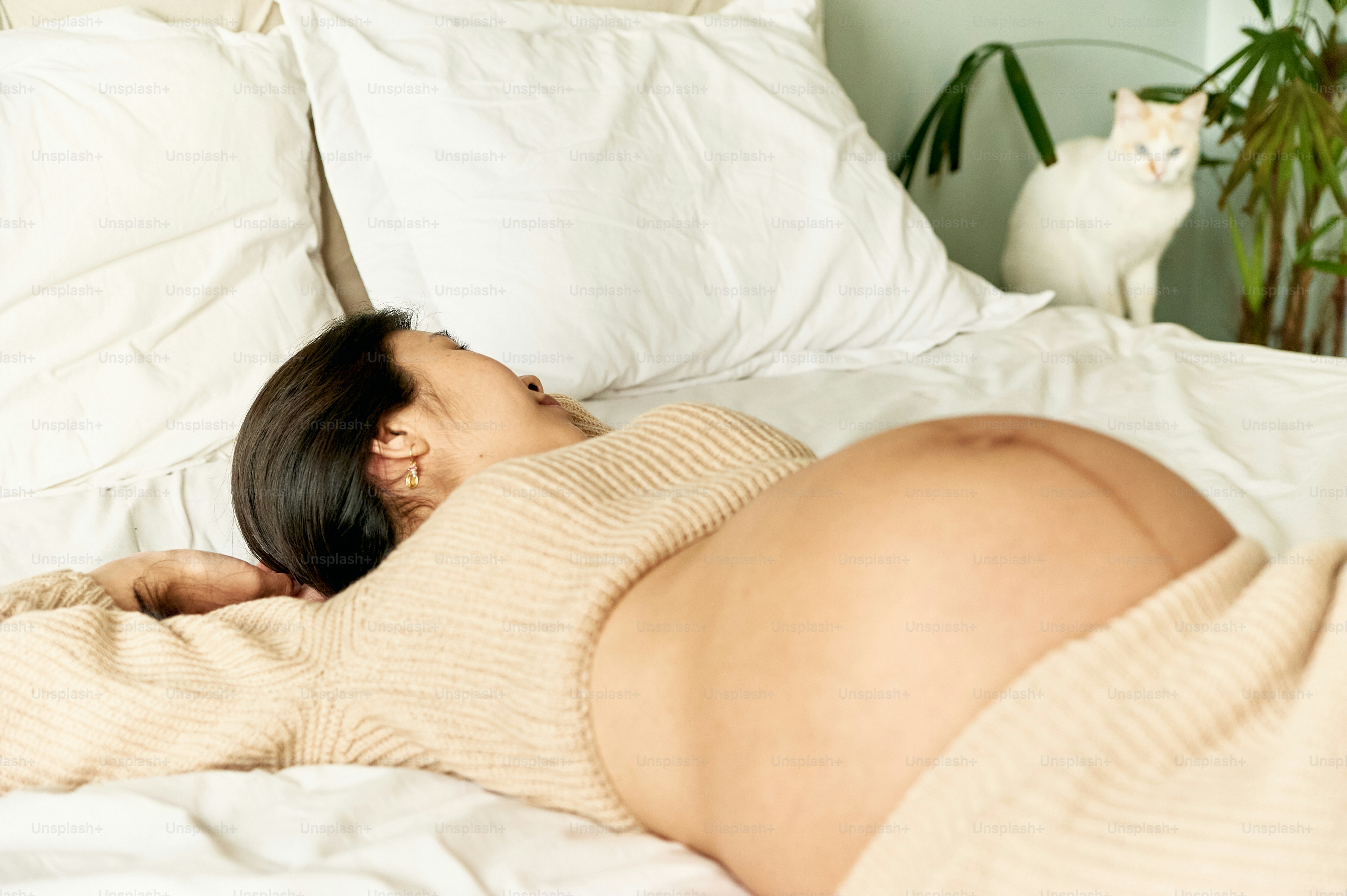 a pregnant woman laying on a bed with a cat in the background
