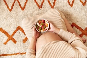 a woman laying on a rug holding a bowl of fruit
