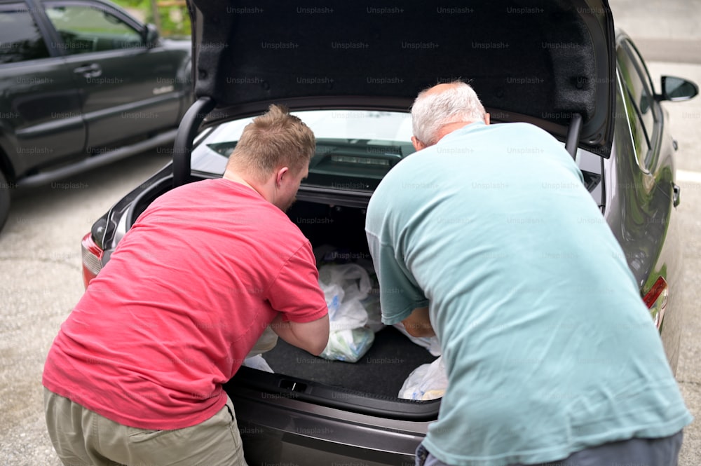 Due uomini che caricano oggetti nel bagagliaio di un'auto