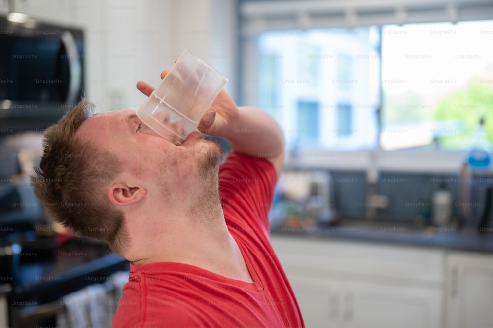 um homem bebendo de um copo de plástico em uma cozinha
