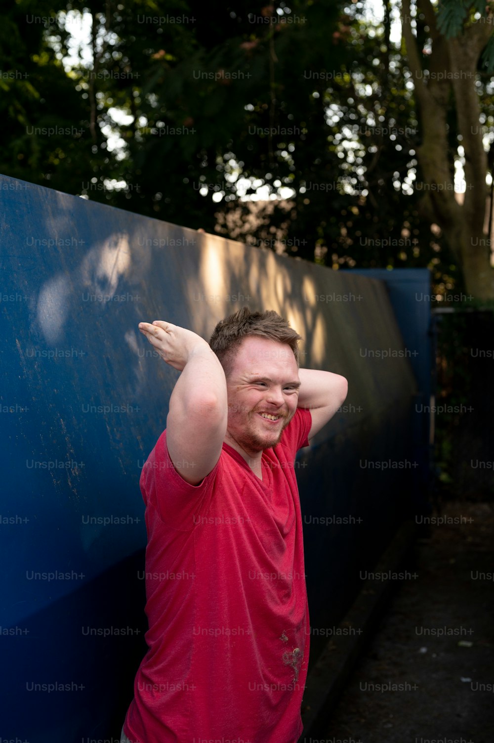 a man in a red shirt leaning against a blue wall