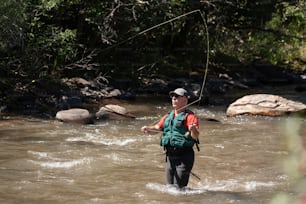 Un hombre parado en un río sosteniendo una caña de pescar
