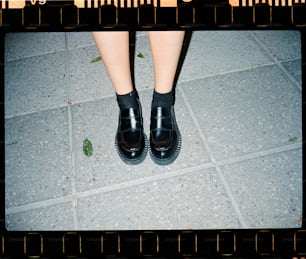 a person wearing black shoes standing on a tile floor